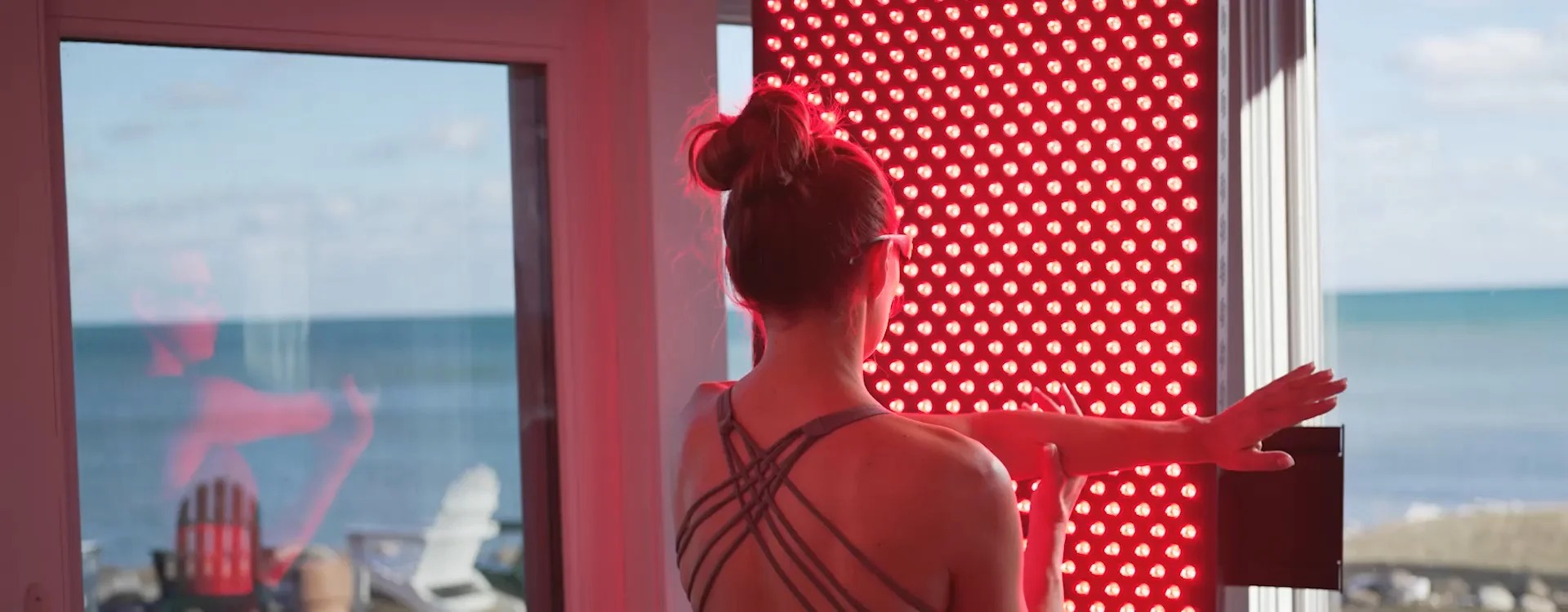 A modern home wellness setup showing a Hooga full-body red light therapy panel and a person using a handheld device on their face ?>